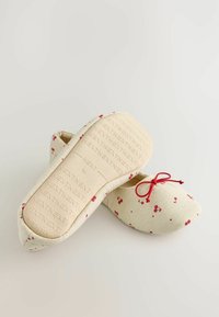 Vaaleanbeige kangassandaalit, joissa on kirsikkakuosi ja punainen nauha. Teksturoitu sisäpohja, jossa on kohokuvioitu brändilogo. Pyöreä kärki.