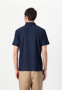 Marinblus med kort ärm, i ett strukturerat ribbat design och klassisk krage. Baksidan visar sömmar och en rak nederkant.