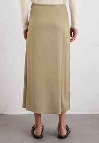 Jupe midi couleur kaki en tissu lisse, dotée d'une taille ajustée et d'une fente sur le côté, associée à des sandales noires plates.