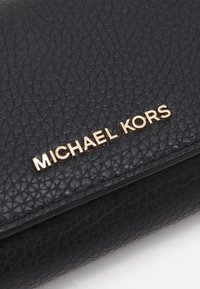 Juodas tekstūruotas odinis piniginė su auksiniu "Michael Kors" logotipu priekyje. Paviršius turi subtilų raštą ir lygų kraštą.