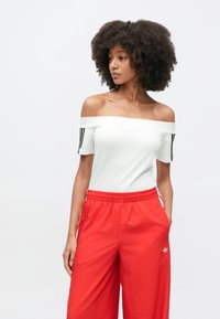 Λευκό τοπ με έξω τους ώμους  και κοντά μανίκια, με τρεις μαύρες ρίγες σε κάθε μανίκι, σε συνδυασμό με φωτεινό κόκκινο, ελαφρύ παντελόνι.