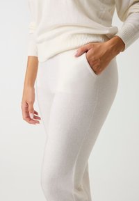 Pull blanc en tricot avec un ourlet côtelé associé à un pantalon doux assorti avec une poche latérale et une texture lisse et légère.