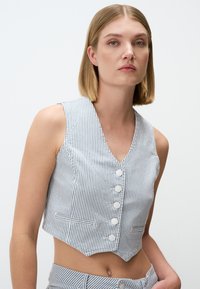 Gestreiftes, tailliertes Top aus Baumwollmischung mit V-Ausschnitt, sechs weißen Knöpfen und Seitentaschen. Das Design ist eng geschnitten und hat einen gezackten Saum.