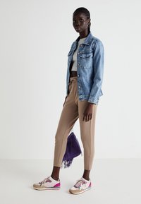 Veste en denim avec poches avant, crop top gris, pantalon beige fuselé, baskets rose et blanche, et sac en daim violet avec cordon de serrage.
