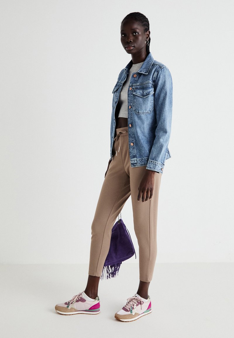 Jeansjacke mit Fronttaschen, graues Crop-Top, beige schmal zulaufende Hose, pink-weiße Sneakers und eine lila Wildleder-Schnürtasche.