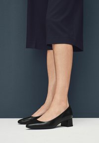 Décolleté nere in pelle con tacco basso, punta affusolata e finitura liscia. Presentano un tacco a blocco modesto e una silhouette elegante.