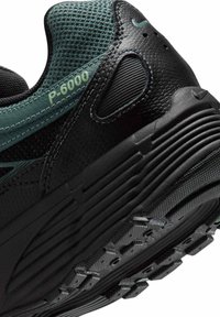 Close-up af sort og grøn P-6000 sneaker med tekstureret sål, mesh-overdel og brandingdetaljer på hæl og side.