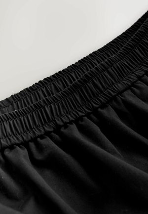 Schwarzer Stoff mit einem gerafften elastischen Bund, der eine glatte Textur und einen dezenten Glanz aufweist. Der Stoff zeigt leichte Falten und Knitter.