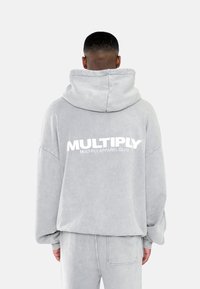Grijze hoodie met een losse pasvorm, voorzien van een groot wit "MULTIPLY" logo op de achterkant, gemaakt van zachte, textuurrijke stof.