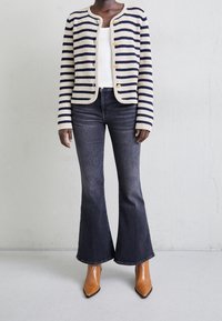 Raidoitu neulejakku vaaleassa ja tummassa sinisessä, yhdistettynä tummiin leveneviin farkkuihin ja teräväkärkisiin vaaleanruskeisiin nilkkureihin. Teksturoitu materiaali ja kultaiset napit.