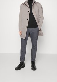 Cappotto grigio chiaro con bottoni, dolcevita nera, pantaloni grigi e stivali Chelsea neri. Tessuto liscio e design su misura.
