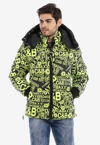 Gepolsterte Jacke in Schwarz mit neongrüner Schrift und Mustern. Sie hat einen hohen Kragen und einen Reißverschluss für zusätzliche Wärme.