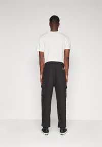 Schwarze Cargo-Hosen mit elastischem Bund und Taschen, kombiniert mit einem hellen T-Shirt. Einfaches Design; getragen mit schwarzen Turnschuhen.