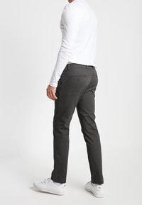 Szare spodnie o prostym kroju, z tylnymi kieszeniami i gładką fakturą, w połączeniu z białą koszulą z długim rękawem i białymi trampkami.