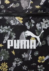 Tessuto nero con motivo floreale che presenta il logo PUMA bianco. Il design include vari fiori in verde, giallo e grigio, con una finitura texturizzata.