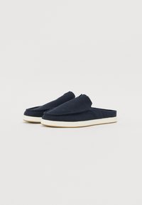 Marineblå canvas tøfler med slip-on design, rund tå og hvit gummisåle. Har sømdetaljer langs kantene.