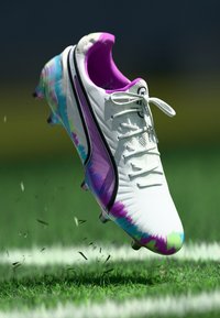 Biele futbalové kopačky s farebnými tie-dye vzormi v purpurove, modrej a zelenej farbe. Majú čierny lem a tradičný systém šnurovania.