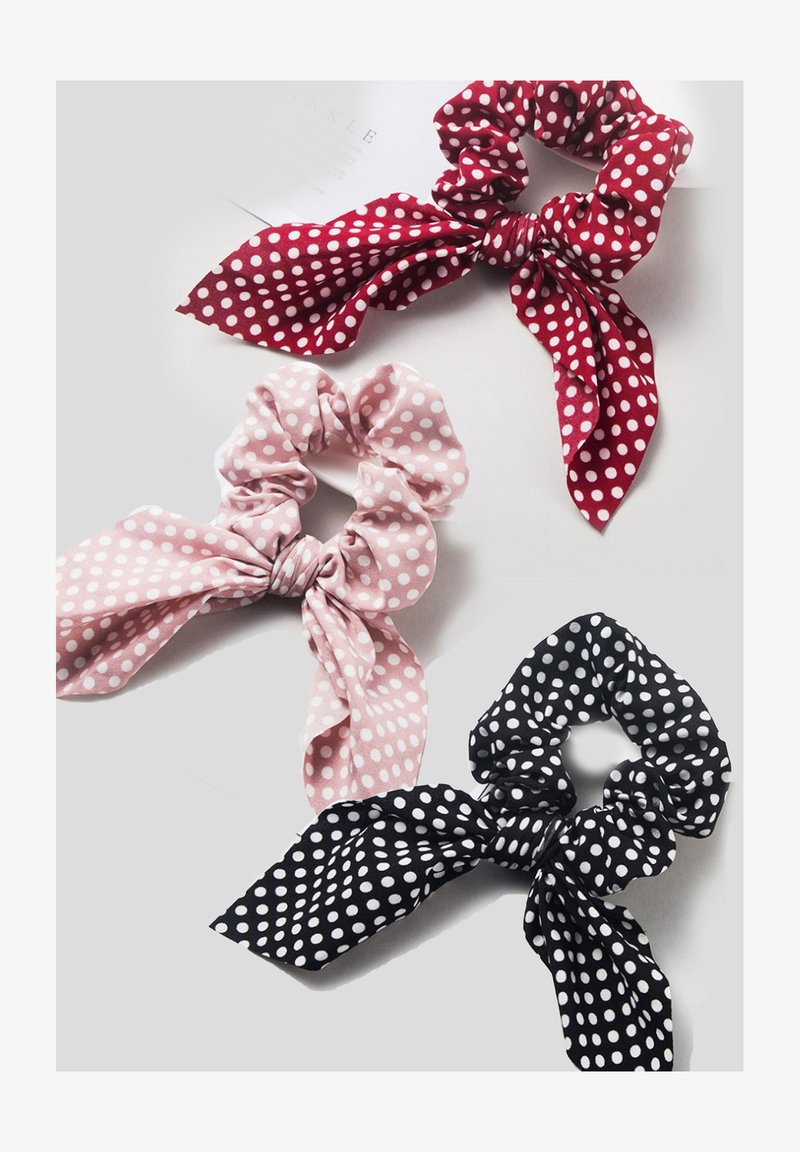 Trīs polka dot skruncīši: sarkans, rozā un melns. Katram ir auduma loka ar mīkstu tekstūru, kas piesiets augšā.