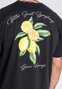 Čierne tričko s akvarelovým dizajnom žltých citrónov a zelených listov. Nápis "Bitter Sweet Symphony" je nad umením.