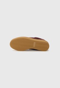 Zapatilla con un upper burdeos, tejido texturizado y una suela de goma acanalada. La suela exterior presenta un patrón en espiga para mejorar la tracción.