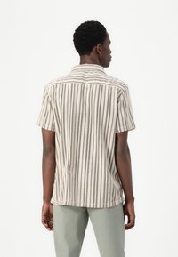 Short-sleeve shirt in beige with vertical stripes and dot patterns. Features a collared neck and a relaxed fit, made from lightweight fabric.
