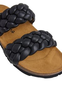 Black braided leather slide sandal featuring two wide straps, a cushioned brown footbed, and a textured black rubber sole.