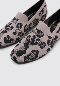 Zapatos beige de tipo slip-on con un material superior de punto texturizado, que presenta un patrón de leopardo negro y un diseño de punta afilada. Suela de goma negra.