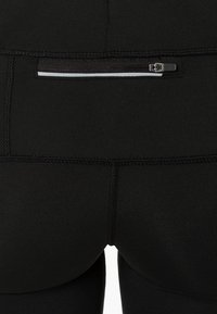 Leggings atléticos negros con una textura suave, que cuentan con un pequeño bolsillo con cremallera en la parte trasera y detalles de costura en contraste.