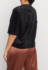 Svart, kortärmad topp gjord av mjukt, sammetsliknande tyg. Rund halsringning och avslappnad passform. Kompletterar ett par rosafärgade satinbyxor.