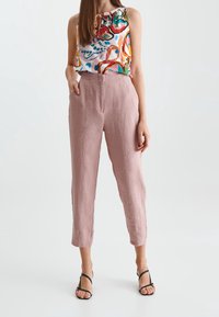 Pantaloni in lino rosa chiaro con vestibilità sartoriale e tasche laterali, abbinati a una blusa in satin multicolore con un scollo arricciato.
