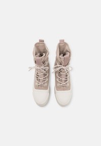 Des sneakers montantes avec un schéma de couleurs beige et crème, un tissu texturé, un capuchon en caoutchouc blanc et des lacets contrastants.