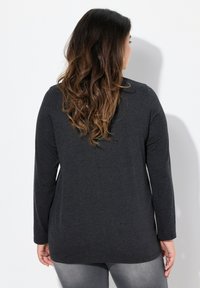 Dunkelgraues Langarmshirt mit lockerer Passform, abgerundetem Saum und weicher Textur, getragen mit grauen Jeans; von hinten gezeigt.