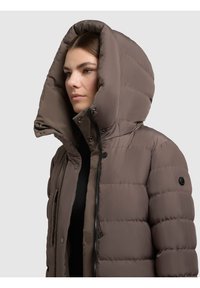 Geacă puf maro, cu glugă mare, închidere cu fermoar și capse, având o textură netedă și un detaliu subtil de cusături pe corp.