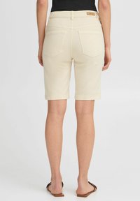 Shorts en denim couleur crème avec une coupe ajustée, dotés de cinq poches et d'une taille cousue. Texture lisse avec un ourlet droit.