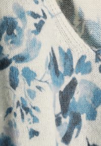 Sweter z dzianiny w kwiatowy wzór, o miękkiej, teksturowanej białej bazie i niebieskich wzorach. Posiada okrągły dekolt i luźny, wygodny krój.