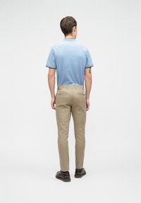 Svetlomodrá polo košeľa s krátkymi rukávmi, v kombinácii s béžovými chinos nohavicami a tmavohnedými topánkami. Minimalistický dizajn, bez viditeľných vzorov alebo log.