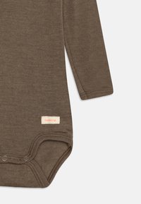 Rjav bodysuit s dolgimi rokavi, izdelan iz teksturirane tkanine, z gumbi na dnu in blagovno oznako s svetlo oranžno besedilo.