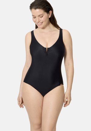 Mujer sonriendo, vistiendo un bañador de una pieza negro sin mangas con un escote en V profundo y detalle fruncido en el centro del frente.