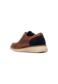 Zapato de cuero marrón con detalles de ante azul marino, diseño de cordones, suela beige y forro interior texturizado con rayas de colores.
