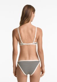 Randig bikini-set i svart och beige. Toppen har justerbara axelremmar och en spänne baktill; underdelen har en solid rem med horisontella ränder.
