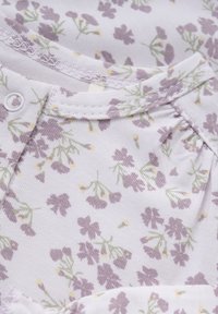 Witte stof met een delicaat bloemenpatroon in lichtpaars en groen. Heeft een knoopsluiting en geplooid detail bij de hals.