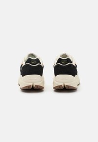 Black and beige sneakers featuring a textured suede upper, thick cream midsole, and rubber outsole with a tread pattern. Brand logo on the heel.