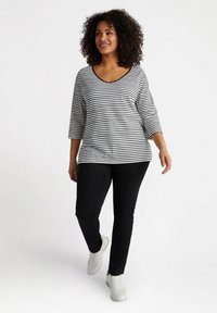 Randig svart och vit topp med trekvartsärmar och V-ringning, kombinerad med svarta byxor och vita sneakers. Slät tygstruktur.