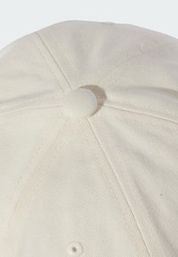 Beżowa czapka bejsbolowa z teksturowanej tkaniny, sześciopanelowa konstrukcja i okrągły guzik na górze. Widoczne szwy wzdłuż szwów.