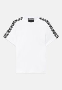 Balta trumpa rankovėmis marškinėliai su juoda prekės ženklu juosta, ant kurios užrašyta "Versace Jeans Couture", einančia per pečius ir kaklo etiketę.