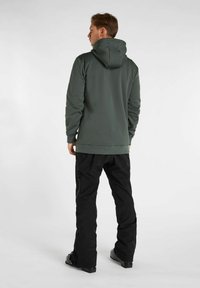 Felpa grigia con design aderente e cappuccio regolabile, abbinata a pantaloni neri con tasche con zip e vestibilità ampia.