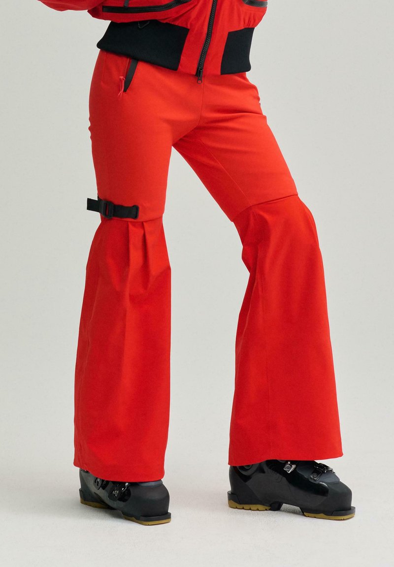 Pantaloni de schi roșii cu tiv evazat, având un detaliu cu cataramă la genunchi. Asortați cu cizme de schi negre și un design de țesătură texturată.