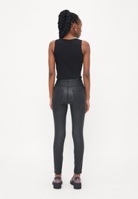 Zwarte mouwloze top gecombineerd met hoge, aansluitende zwarte broek. Glad materiaal met subtiele naden en twee achterzakken. Zwart schoeisel.