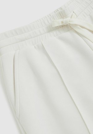 Biele jogger nohavice vyrobené z mäkkej tkaniny, s elastickým pásom, šnúrkovým zapínaním a bočnými vreckami s detailom záhybov.