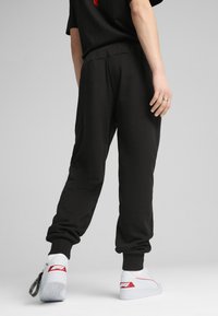 Czarne spodnie dresowe z elastycznym pasem i ściągaczami u kostek, w połączeniu z białymi sneakersami z czerwonymi akcentami i teksturowanymi sznurowadłami.